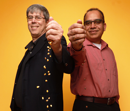 Asheesh Singh and Pat Schnable stand in front of a gold background dropping seeds